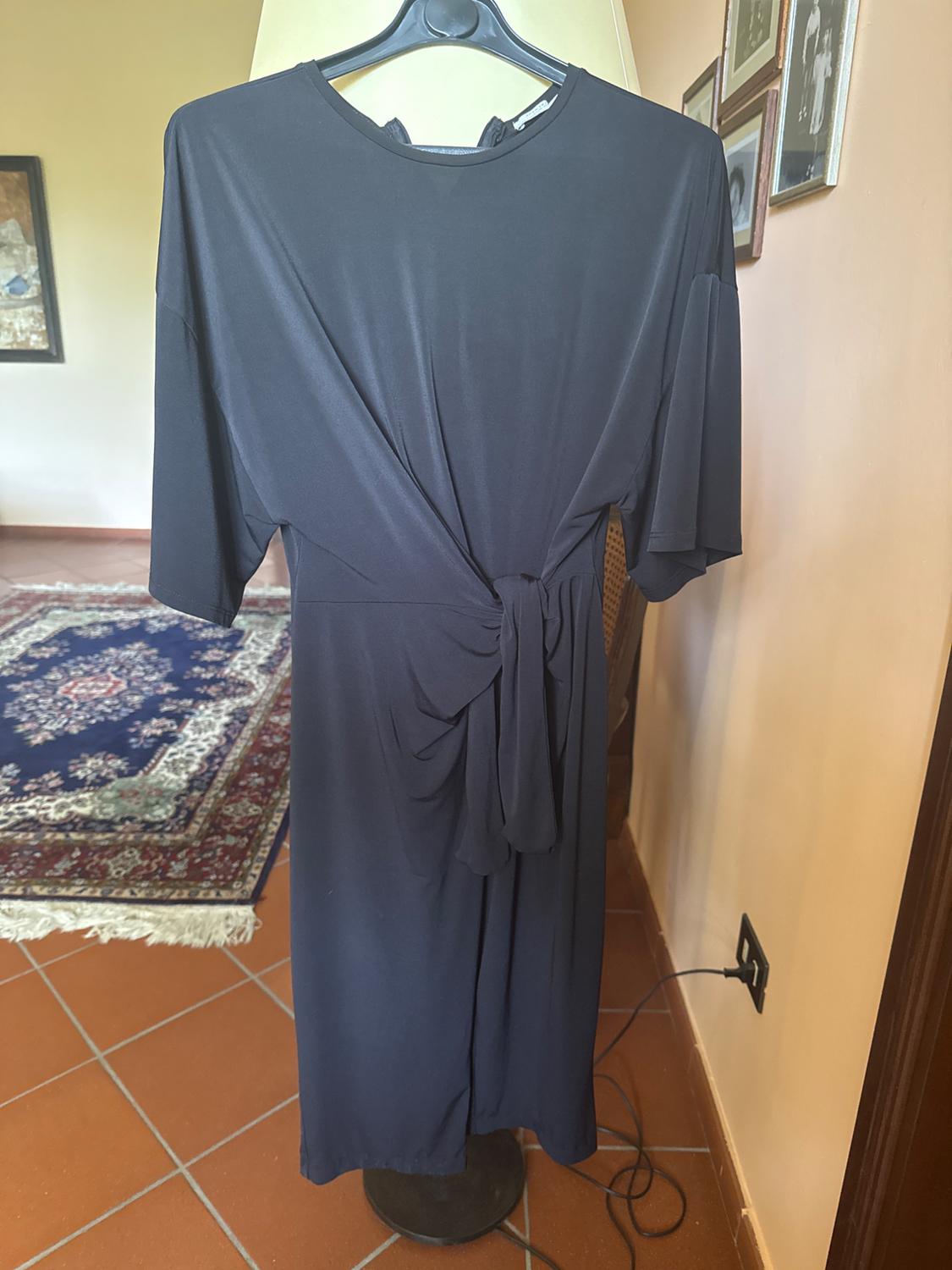 Short-sleeved black dress with a knot at the waist, hanging on a coat hanger in an interior with a tiled floor and a patterned rug.