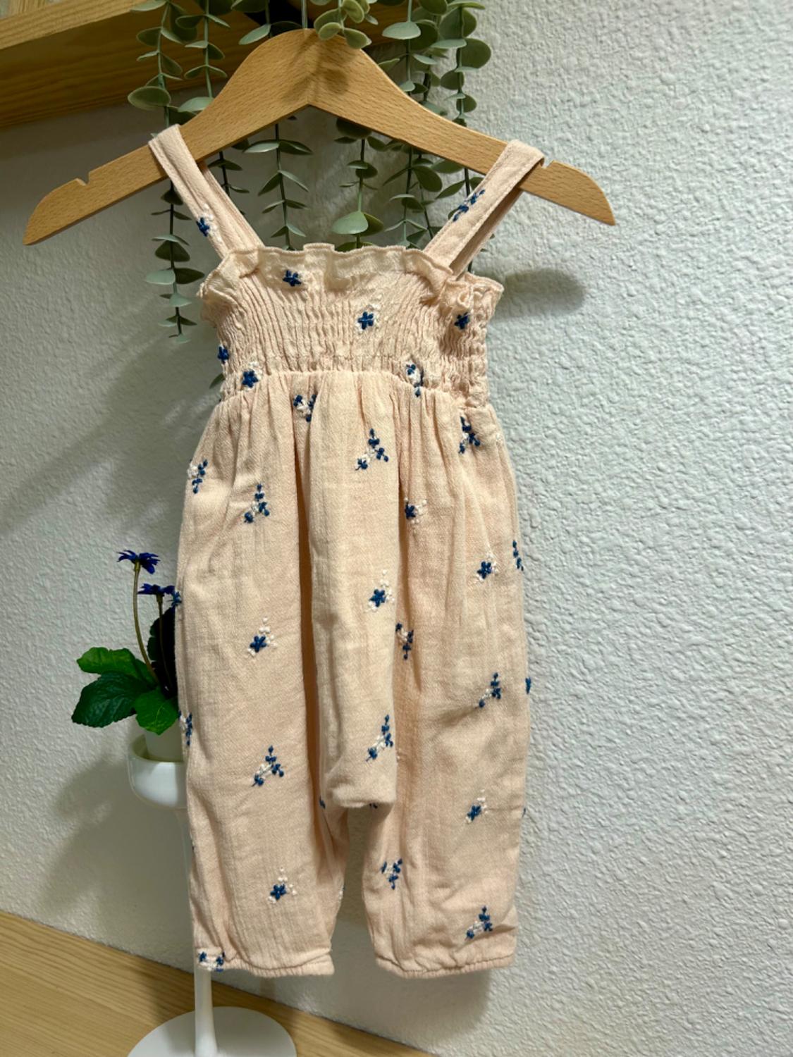 Front view of a beige babygrow with straps and a blue floral print.