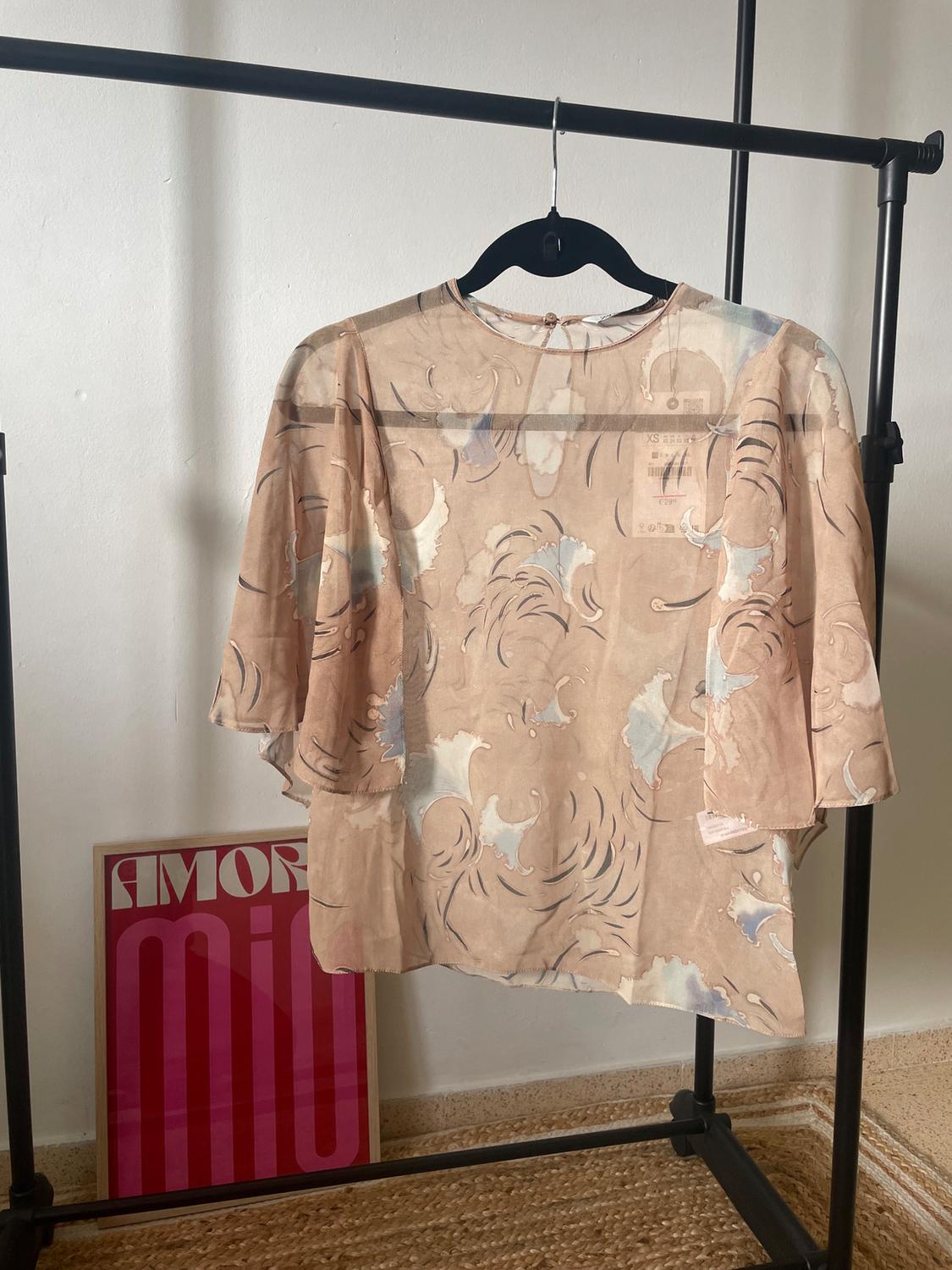 Beige blouse with an abstract print, hanging on a black clothes rail. In the background, a pink sign with the text "My LOVE".