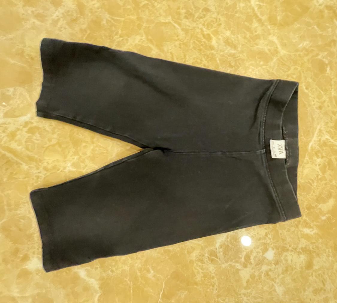 Dark grey short leggings on a yellow marble surface. White label on the waistband with the text ZARA.