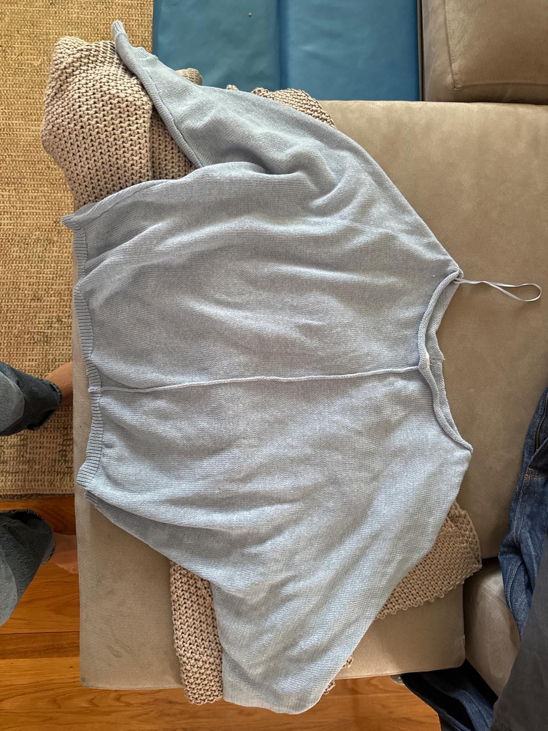 Light gray knit sweater on a beige sofa, with a visible chunky knit texture underneath. Wood and carpet background.