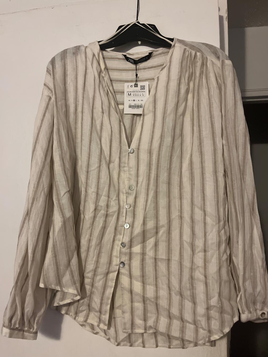 Vertical striped shirt in beige and white tones, hanging on a black hanger. Visible label with size M.