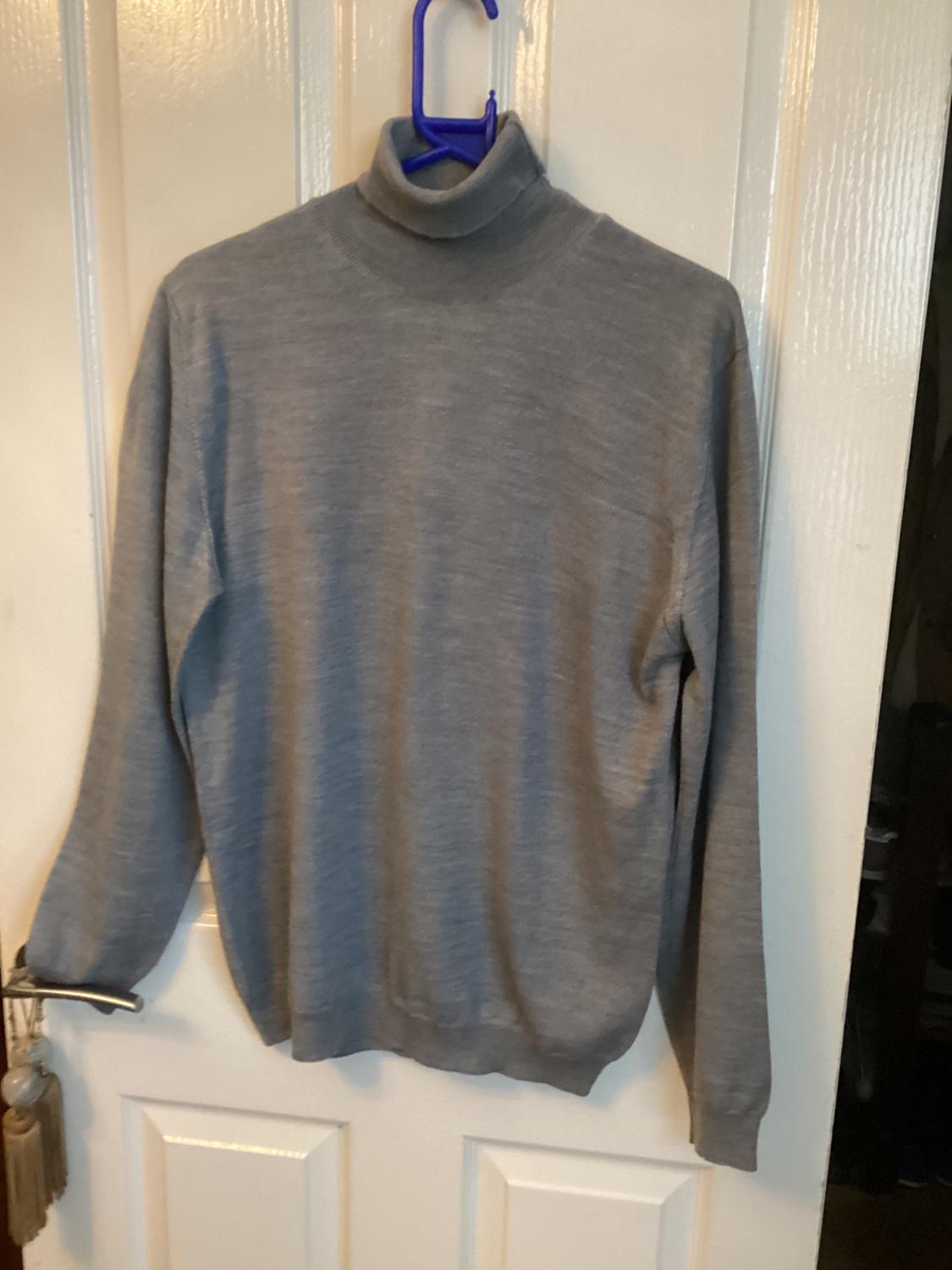 Grey roll-neck jumper hanging on a blue hanger over a white door.