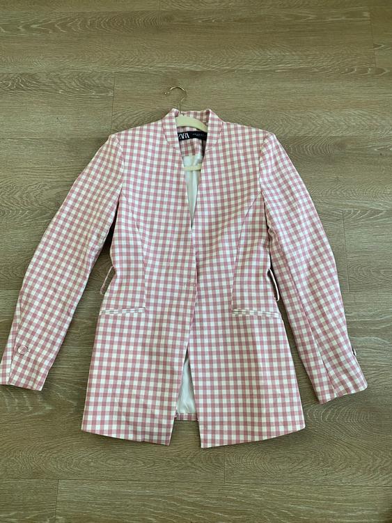 Pink and white plaid jacket hanging on a wooden floor. Label visible on the inside of the collar.