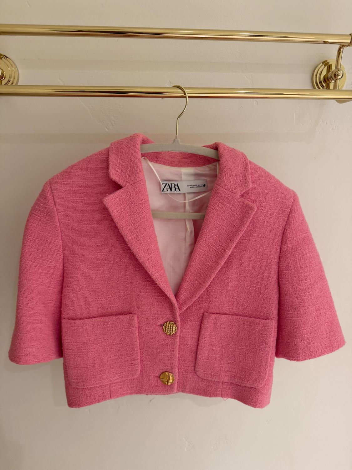 Pink short jacket with lapels and two gold buttons, hanging on a gold hanger. Visible tag: ZARA.