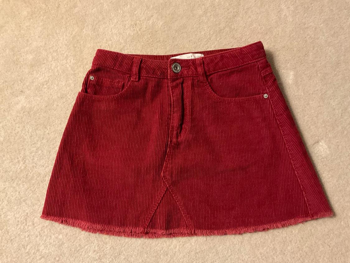 Red corduroy mini skirt with front pockets and frayed hem, on a beige background.