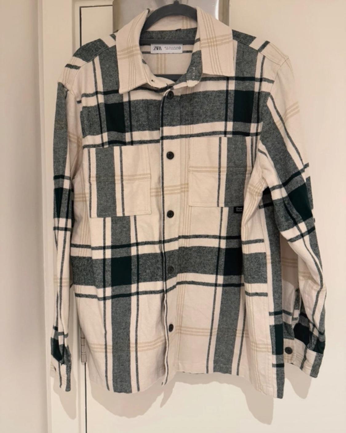 White and green checked long-sleeved shirt with front pockets, hanging on a hanger. ZARA label visible on the collar.