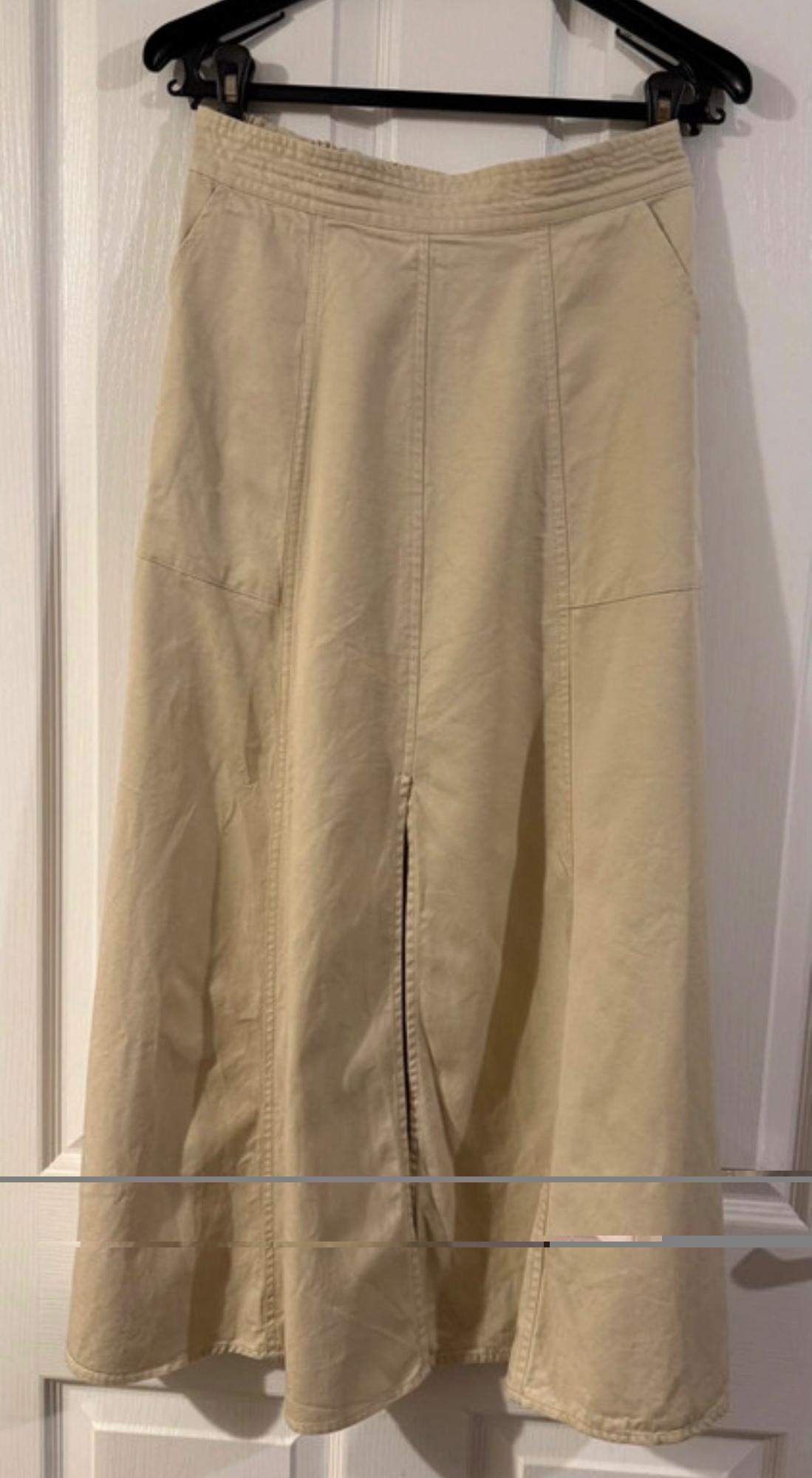 Long beige skirt hanging on a black hanger over a white door. Design with visible seams and a front slit.