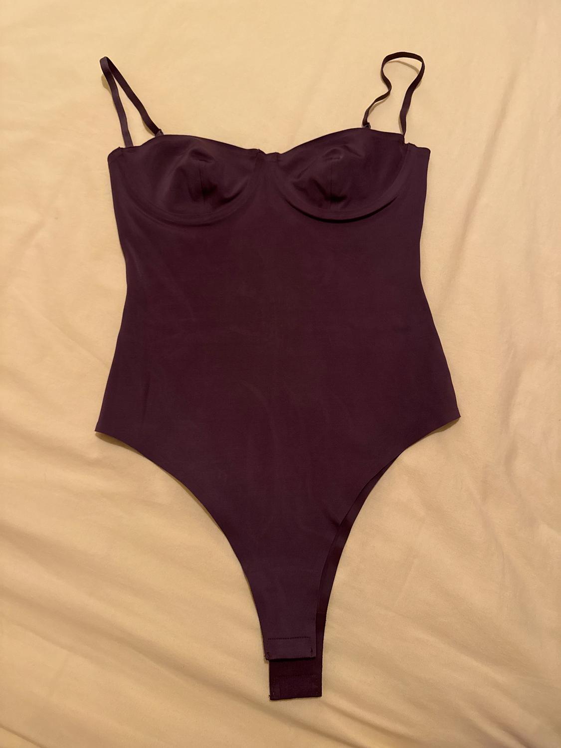 Black bodysuit with thin straps and structured cups, on a beige surface.