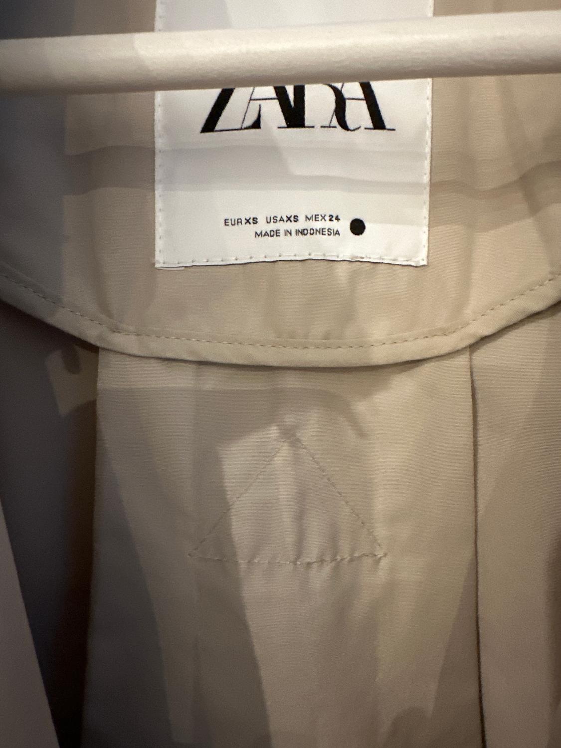 Ετικέτα από ένα μπεζ ρούχο με το λογότυπο της ZARA. Αναγράφει μεγέθη EUR XS, USA XS, MEX 24 και "MADE IN INDONESIA".