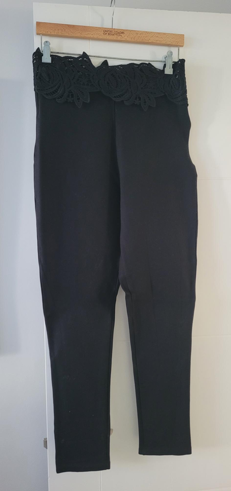 Black trousers with a lace detail on the waist, hanging on a wooden hanger from United Colors of Benetton.