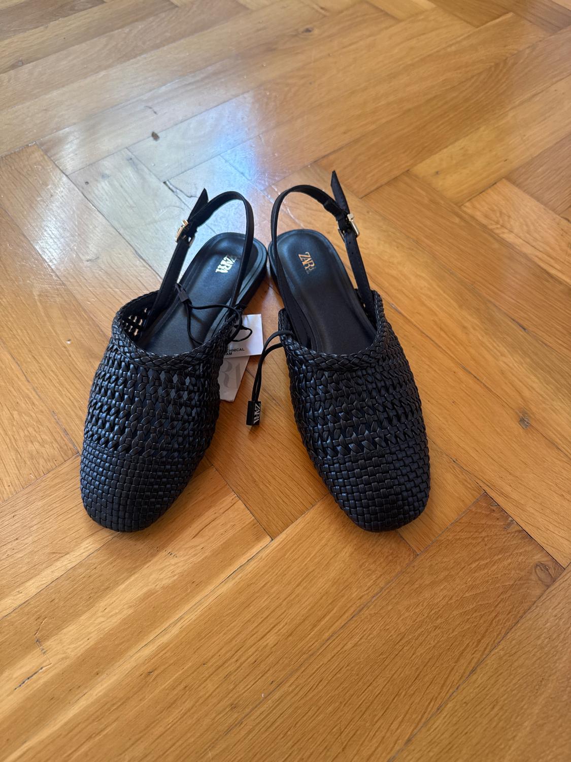 Black mesh shoes with adjustable straps on a wooden floor. Visible label with the text "ZARA".
