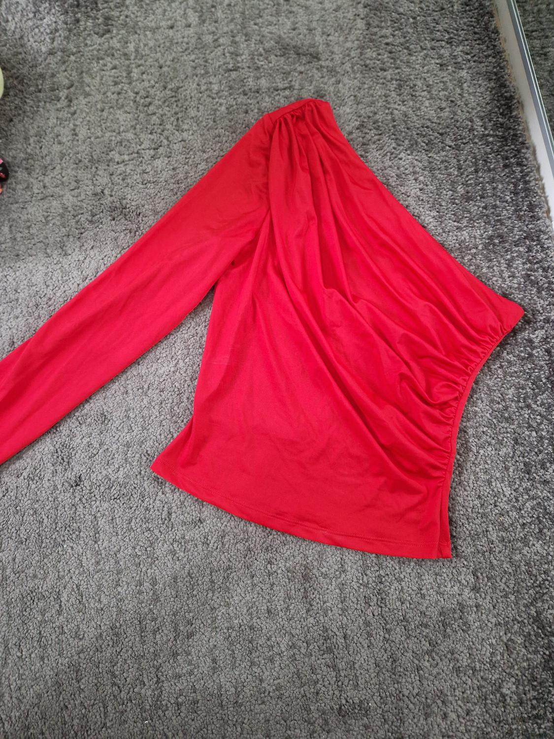 Red asymmetric long-sleeved gathered top, placed on a textured grey rug.