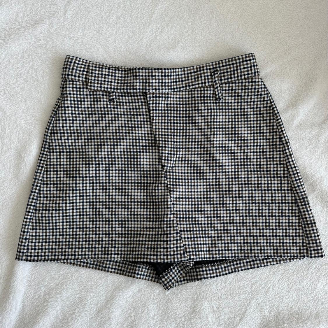 Short skirt-pants with a black-and-white checkered print, belt-loop detail, against a textured white fabric background.