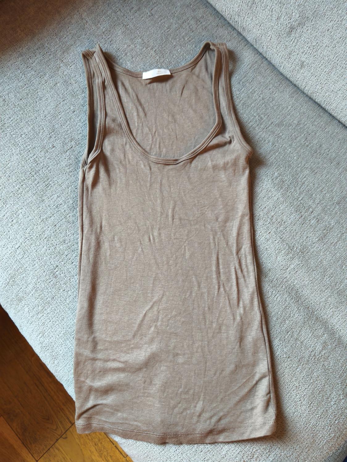 Beige vest top on a grey sofa, viewed from above. The fabric has a soft and slightly wrinkled appearance.
