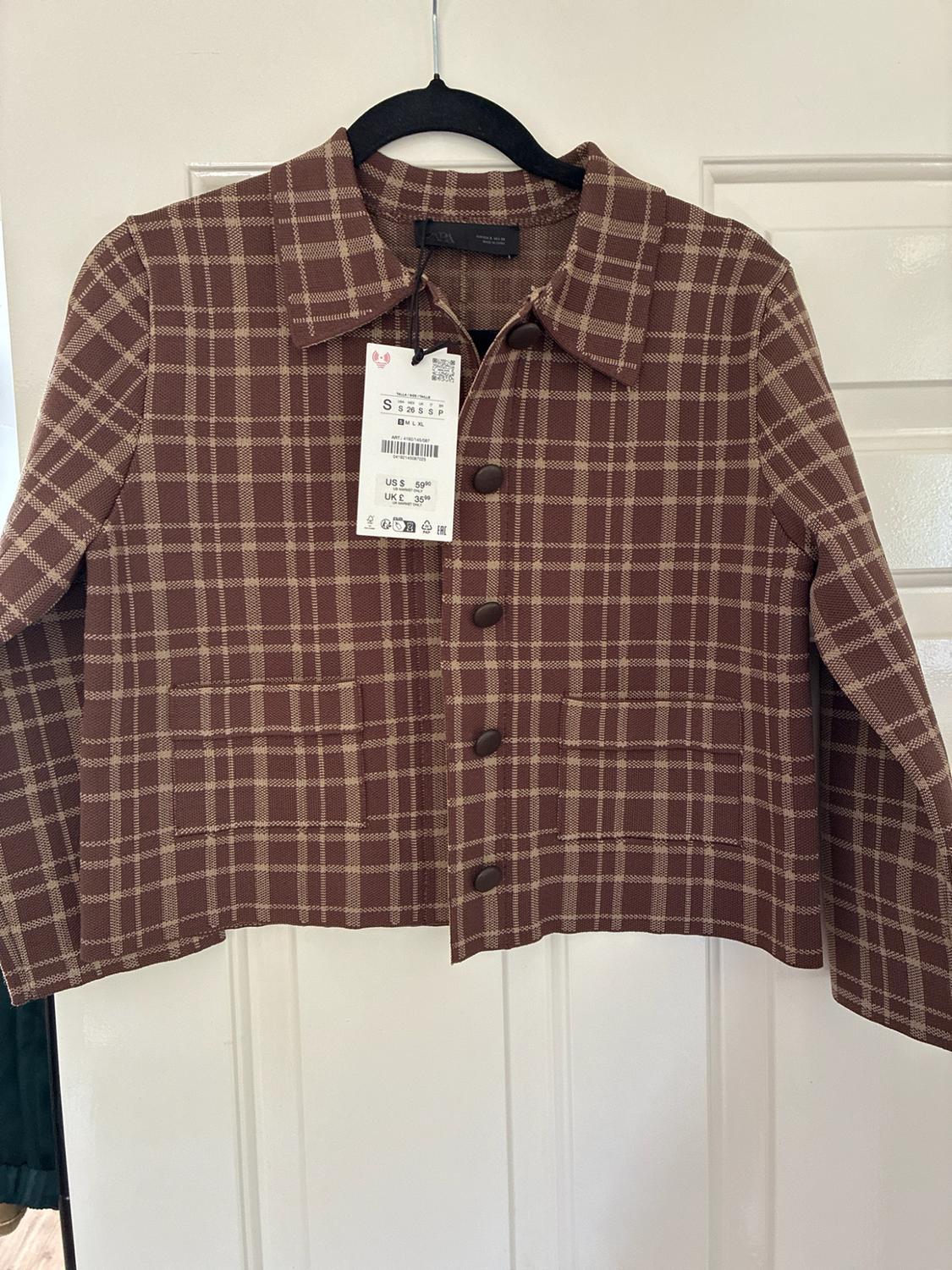 Brown and beige checked jacket with buttons and pockets, hanging on a white door. Text: ZARA S US $ 59.90 UK £ 35.99.