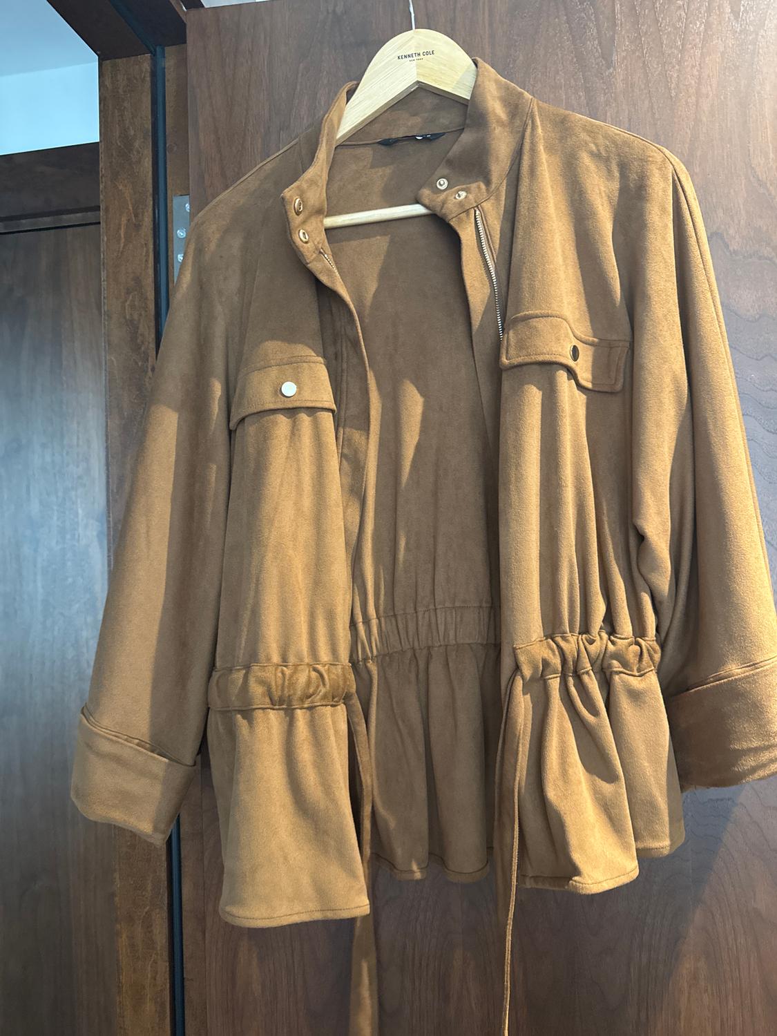 Light brown jacket hanging on a wooden hanger with "Kenneth Cole" brand, dark wood background.