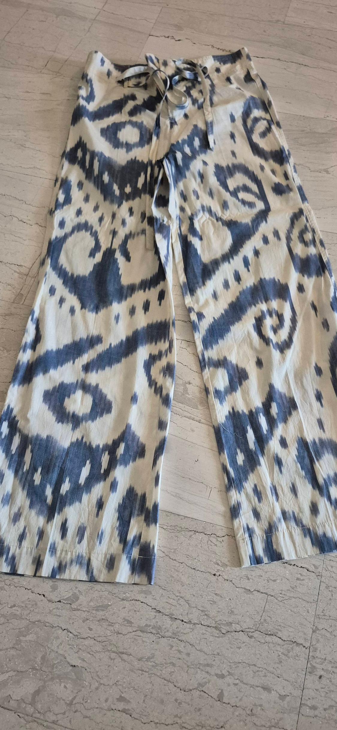 Wide-leg trousers with blue and white print, abstract design, waist tie, on a light marble floor.
