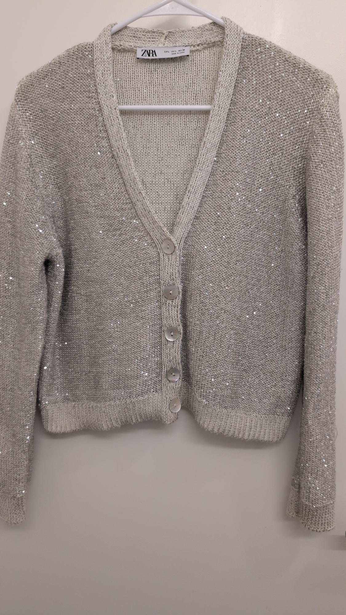 Gray cardigan with sequins and large buttons, hanging on a white hanger. Visible tag with text "ZARA".