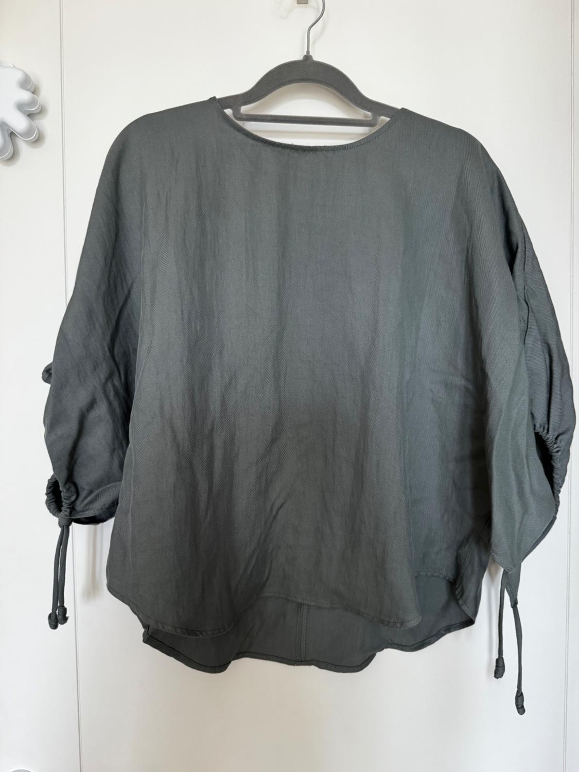 Grey long-sleeved top with adjustable drawstring sleeves, hanging on a black hanger against a white background.