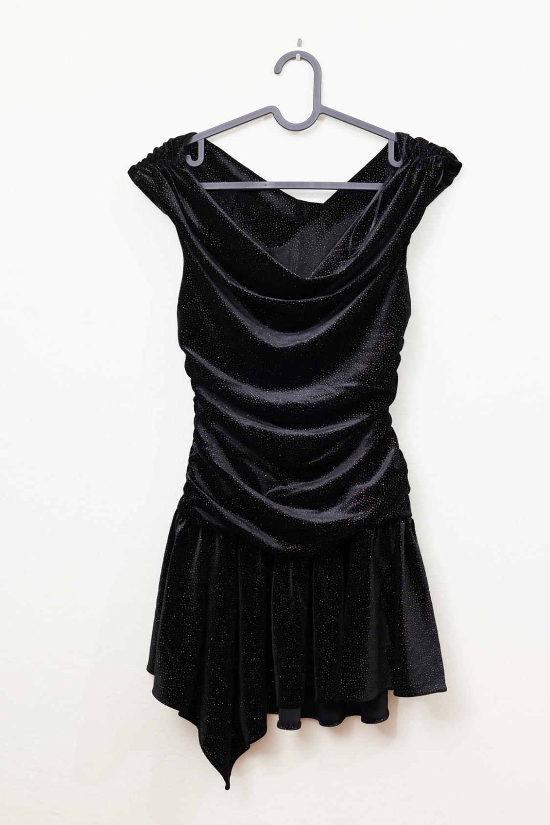 Black short dress with a shiny finish, draped neckline, and a flared skirt, hanging on a gray hanger against a white background.