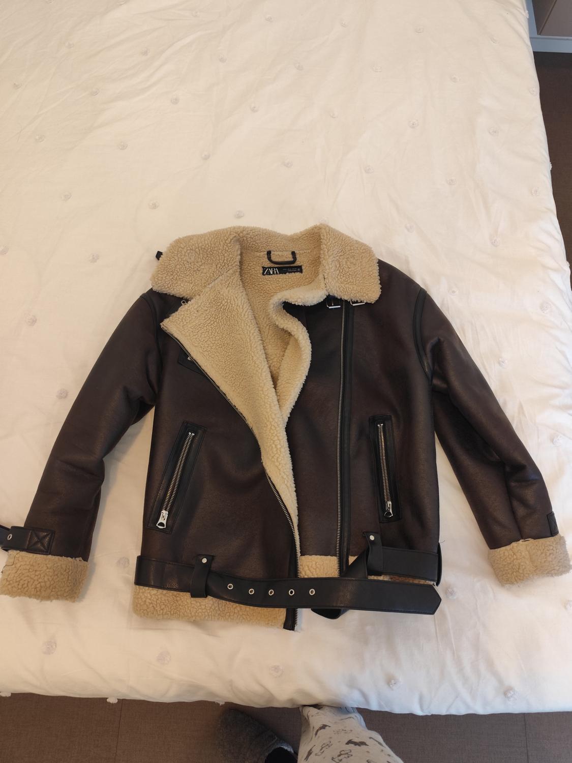 Brown jacket with a beige sheepskin lining and a belt, on a white bed. Visible label: ZARA.