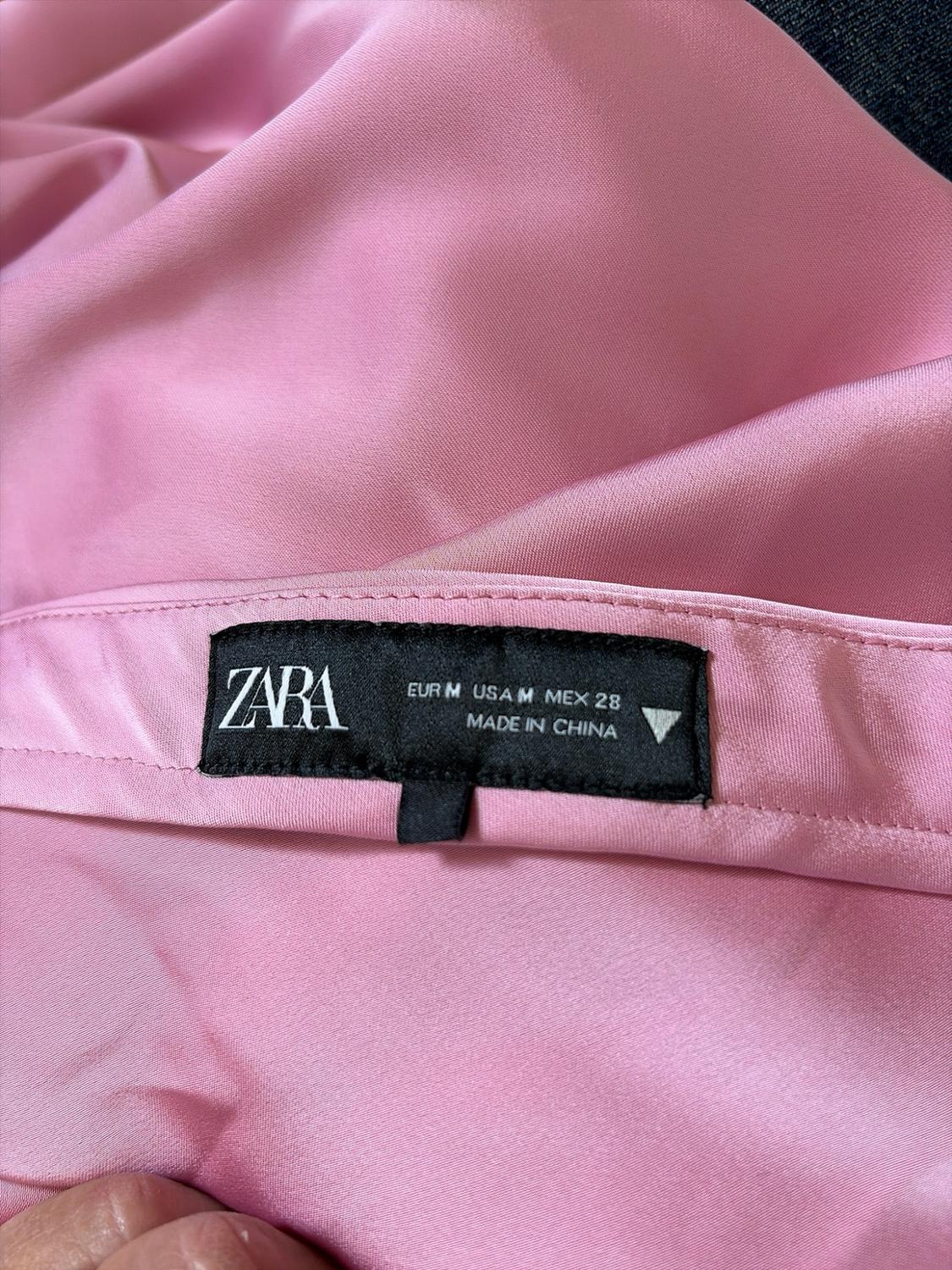Detail of pink satin fabric with a black label that reads ZARA EUR M USA M MEX 28 MADE IN CHINA.