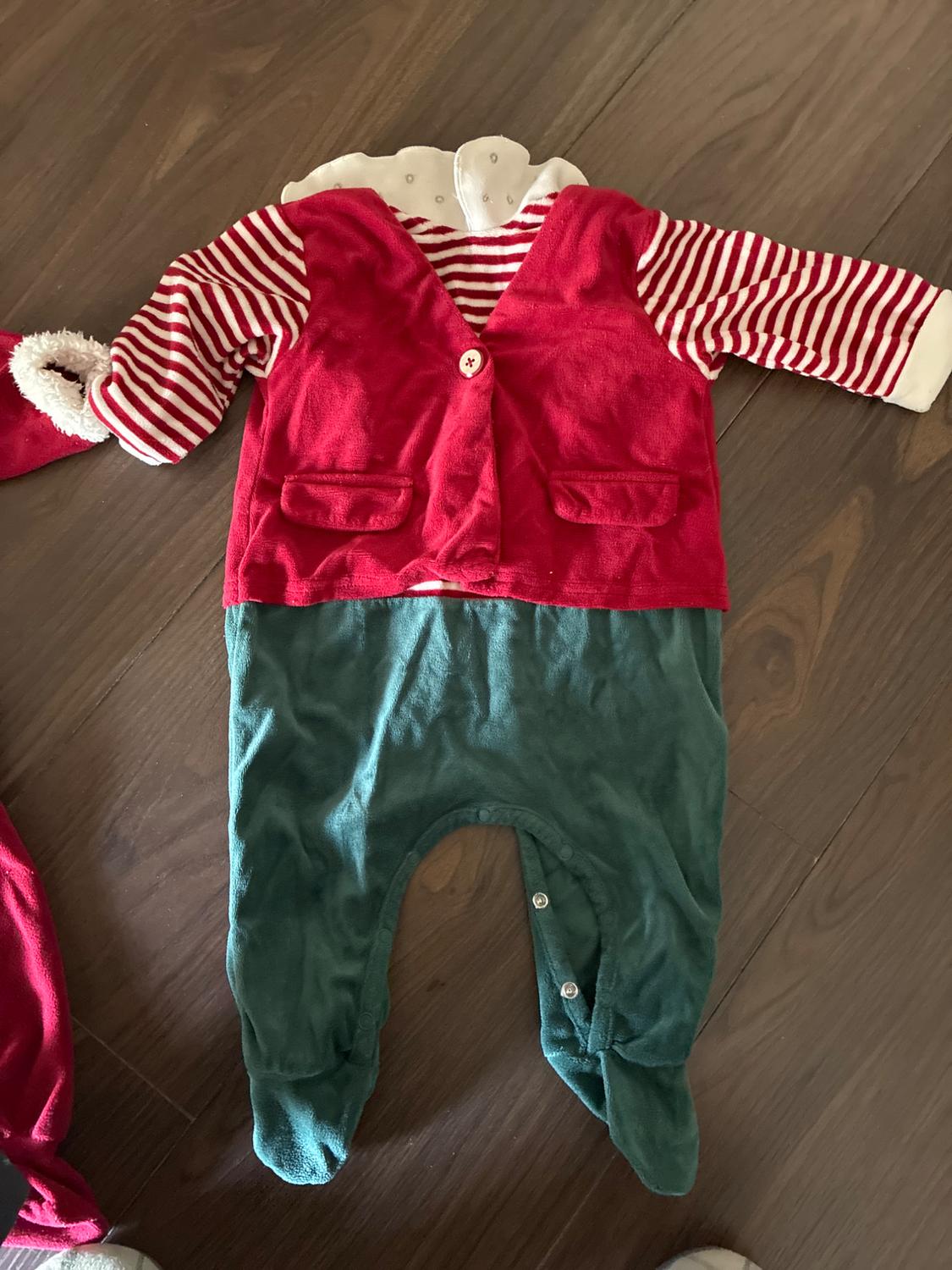 Babygrow laid out on a wooden floor. It features a red body, red and white striped sleeves, and green trousers with feet.