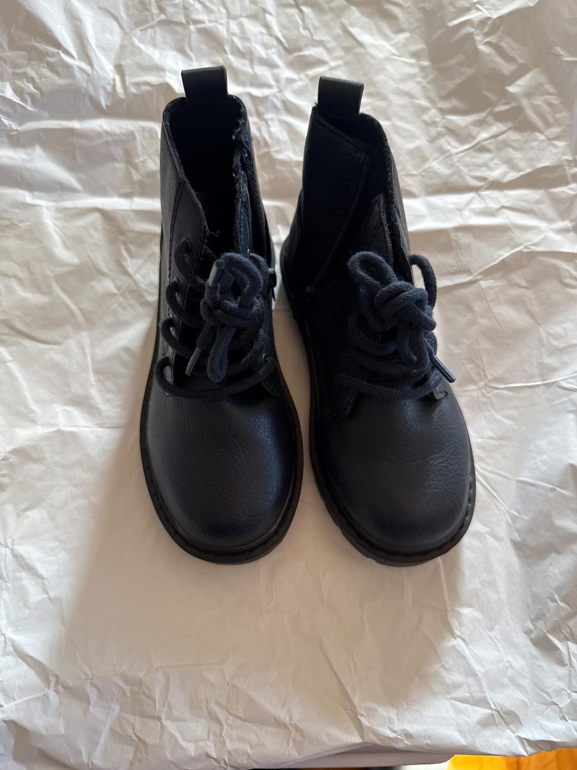 Black leather lace-up boots on white crumpled paper. Top view, showing texture and design details.