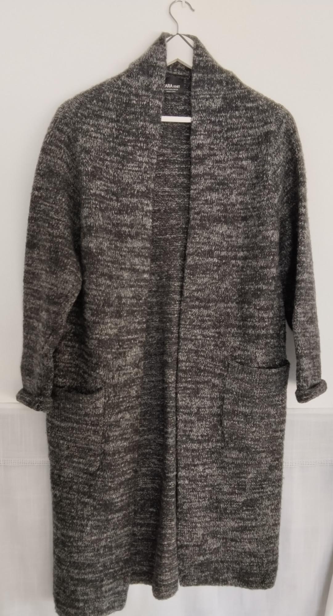 Long open-front grey marled-knit cardigan hanging on a hanger against a white background. Its pockets and the ZARA KNIT label stand out.