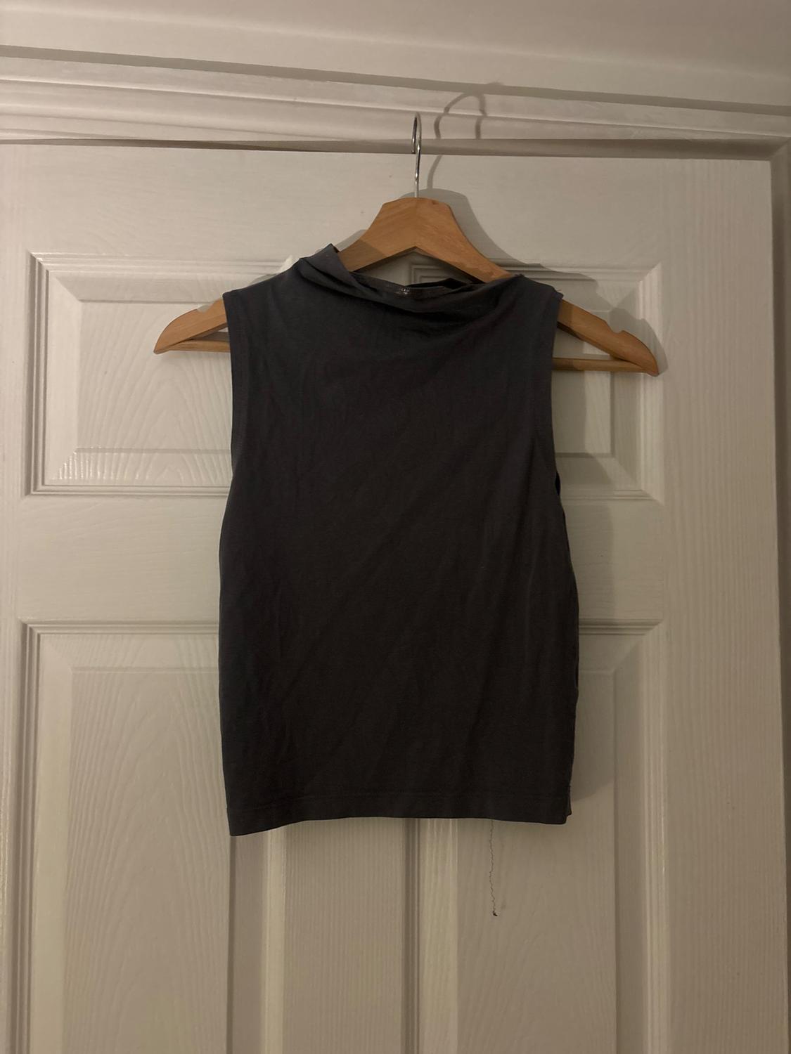 Dark grey sleeveless t-shirt hanging on a wooden hanger over a white door.
