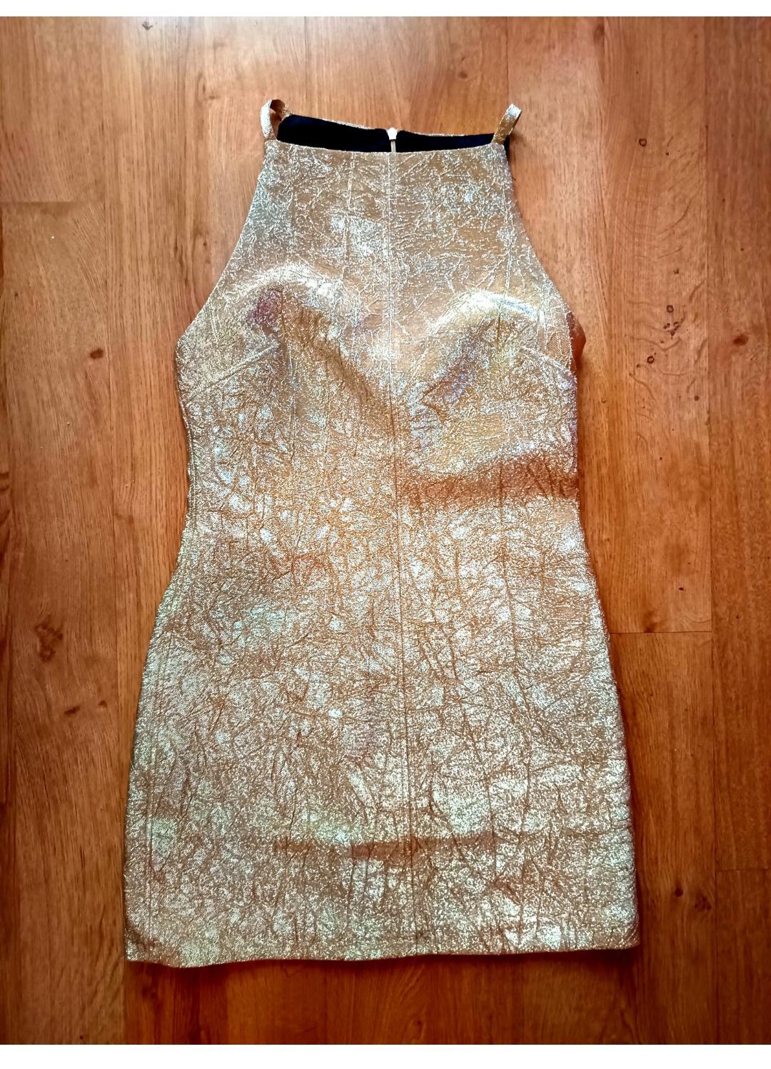 Sleeveless, sparkly gold dress on a wooden floor. Figure-hugging design with a crinkled texture and fastening at the top.