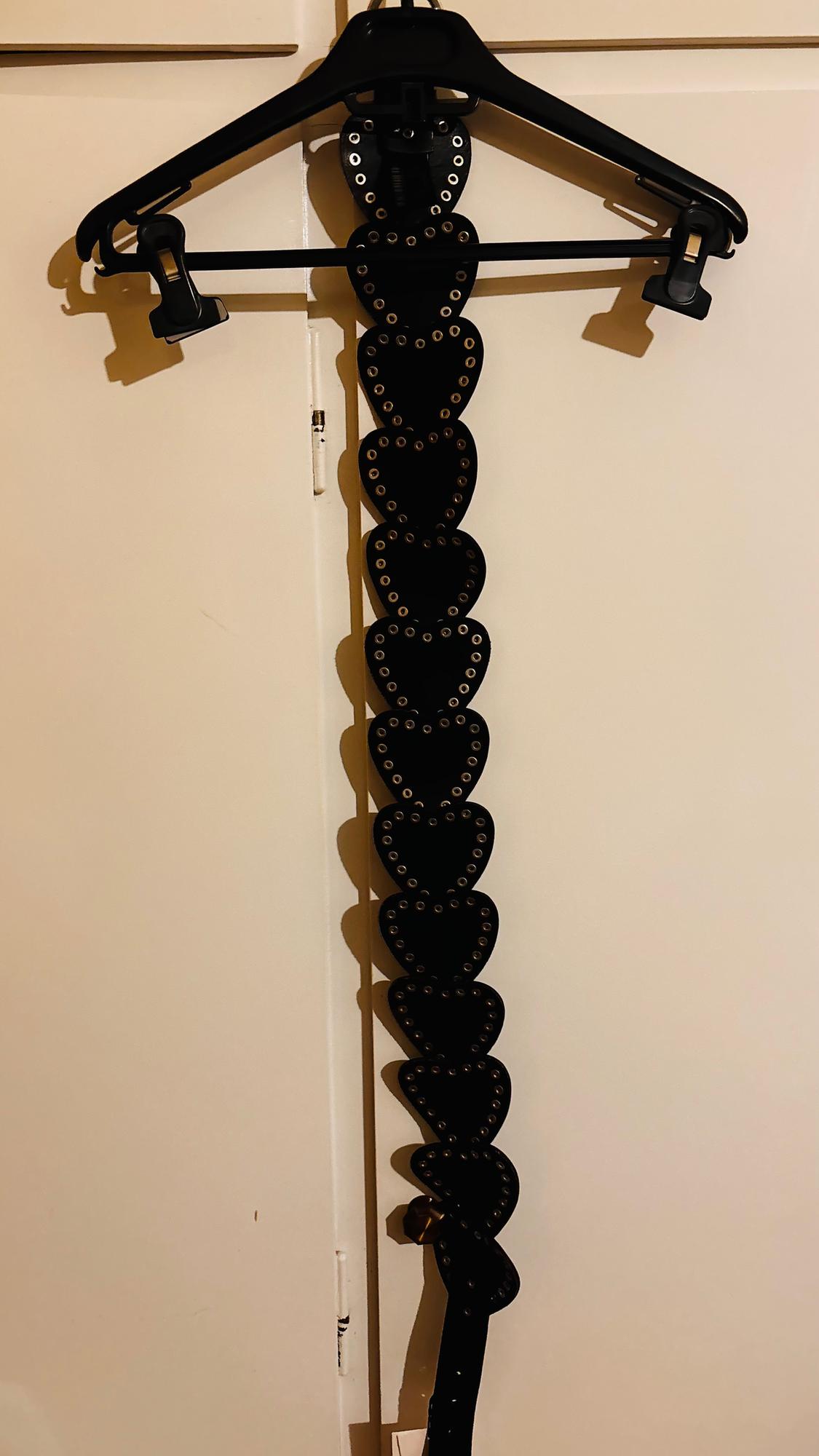 Black belt with heart-shaped metal eyelets hanging on a black hanger over a white door.
