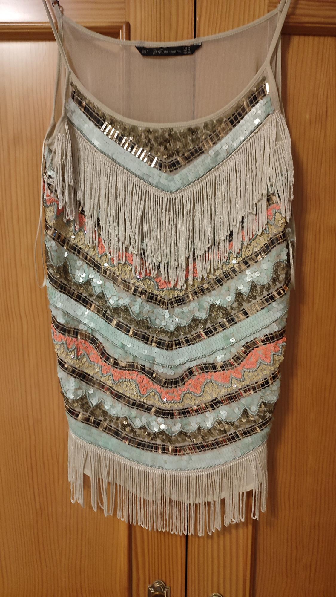 Front view of a dress with fringe and sequins in beige, coral, and mint green tones.