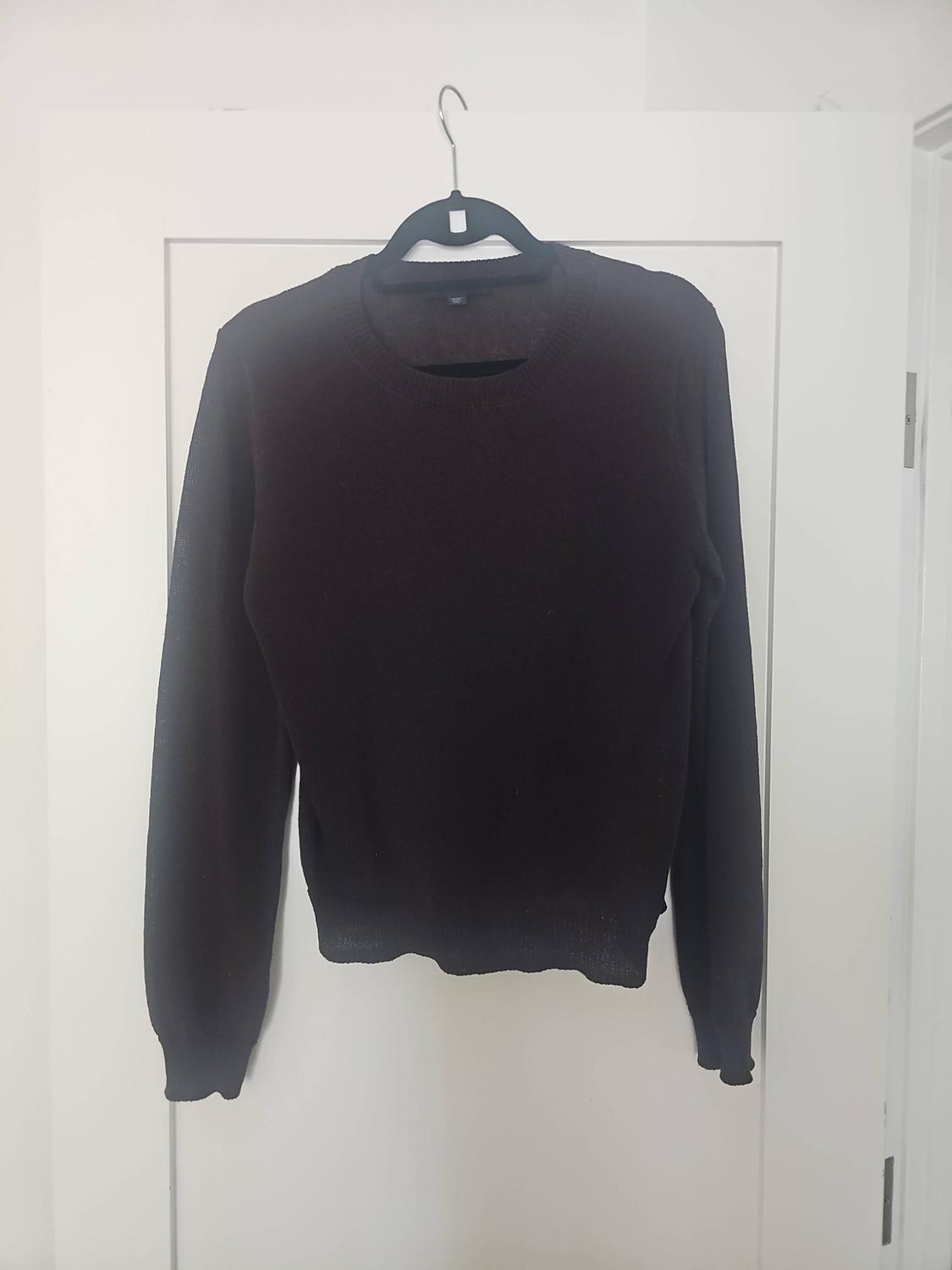 Dark long-sleeved, round-neck jumper hanging on a black hanger over a white door.