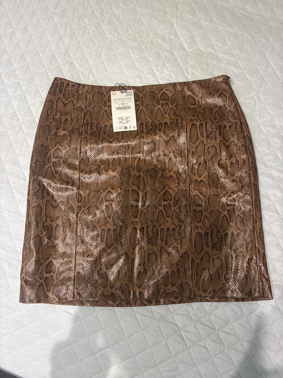 Brown snake print mini skirt on a quilted white bedspread. Visible label with price and size.
