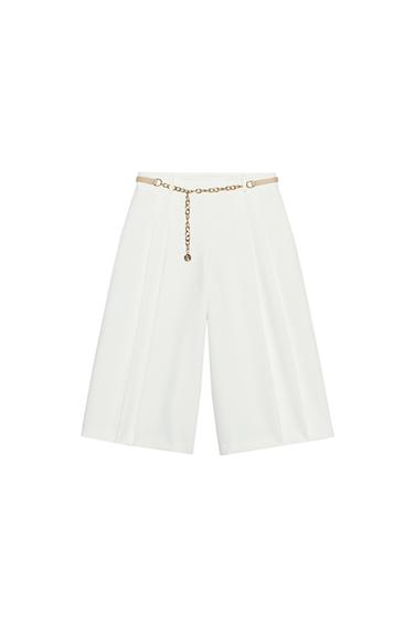 Front view of white trousers with gold chain belt and pleats.