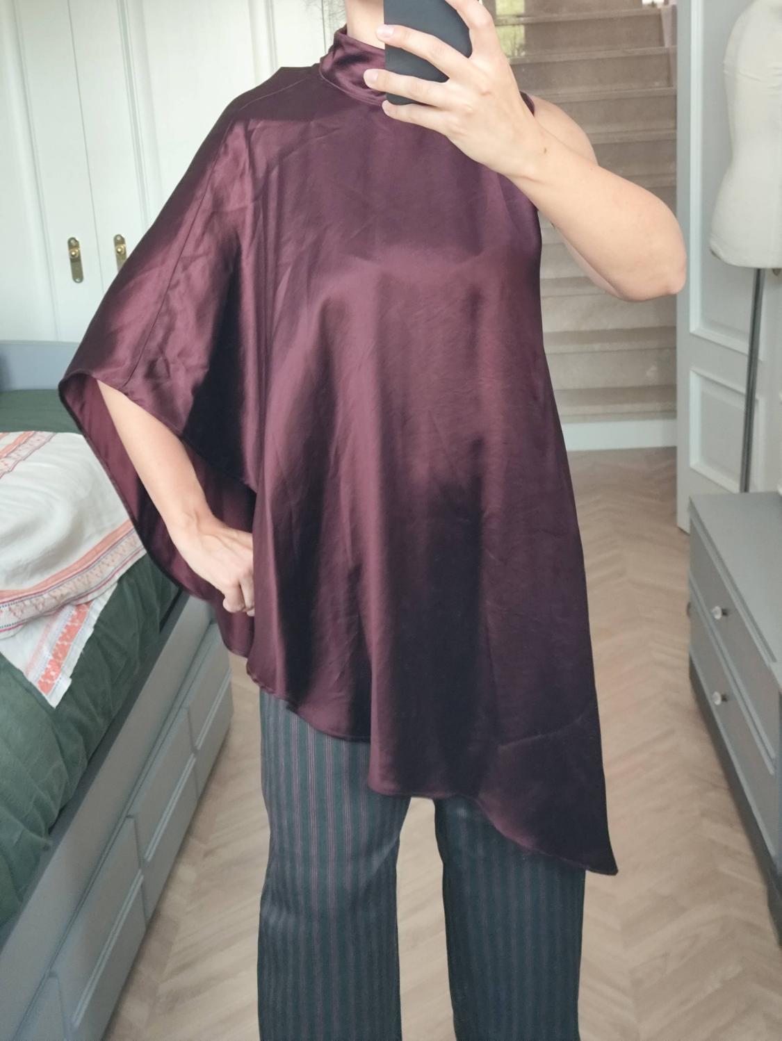 Woman taking a selfie in a mirror. She is wearing a burgundy satin asymmetric high-neck top and pinstripe trousers.