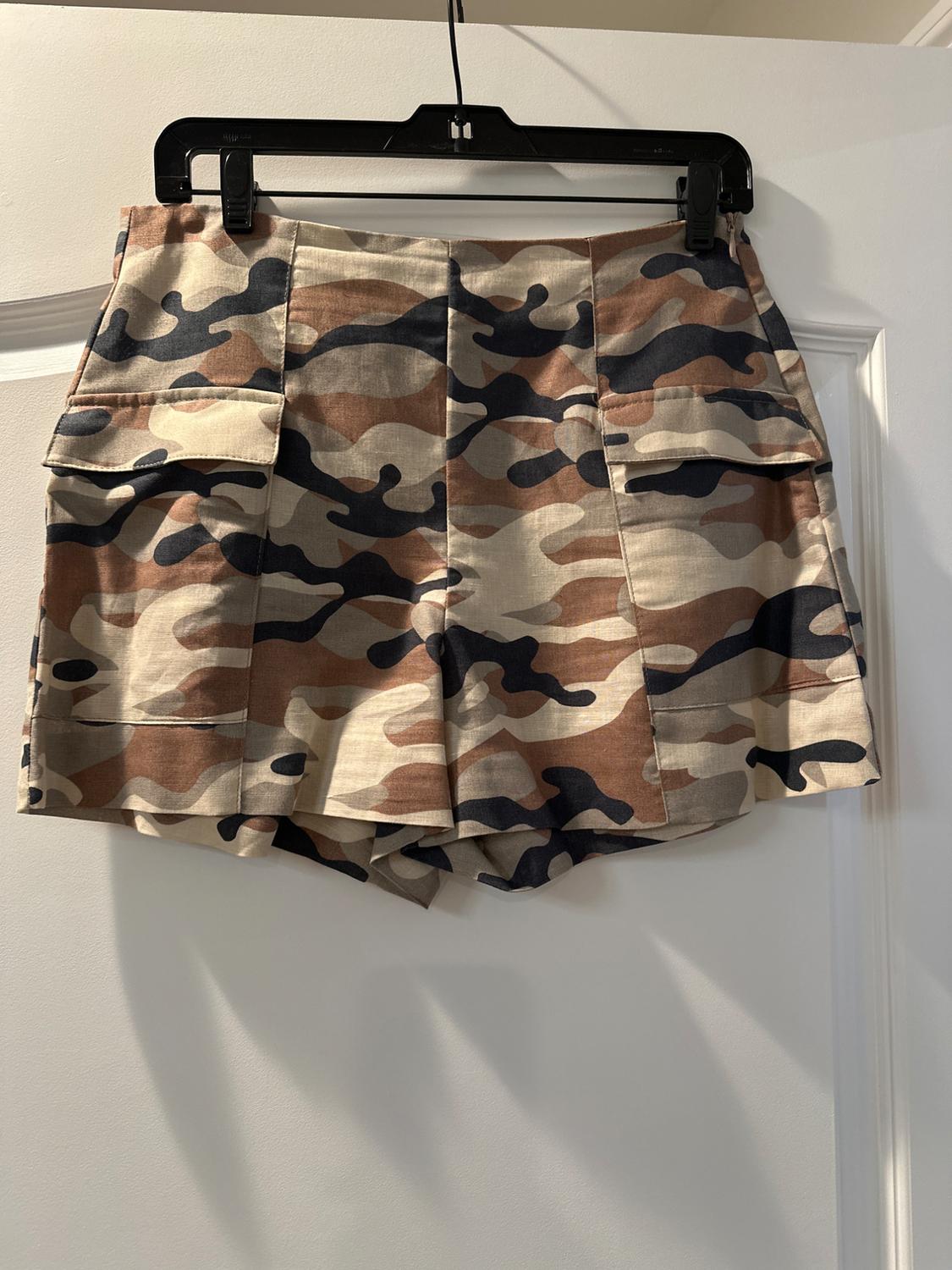 Camo shorts hanging on a black hanger over a white door. Brown, beige, and black tones.