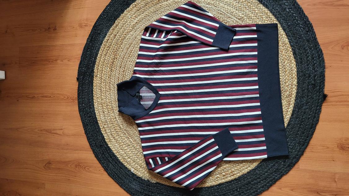 Horizontal striped jumper in blue, red, and white on a round jute rug on a wooden floor.
