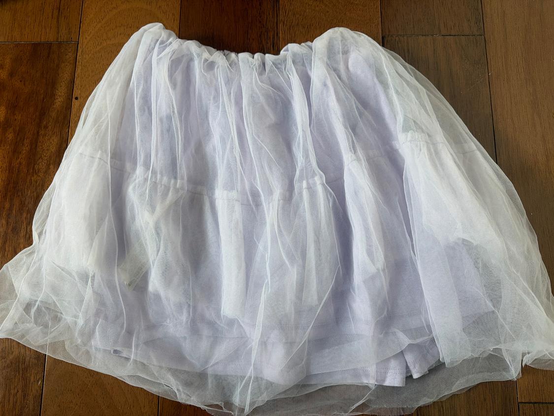 White tulle skirt with several layers, placed on a brown wooden floor.