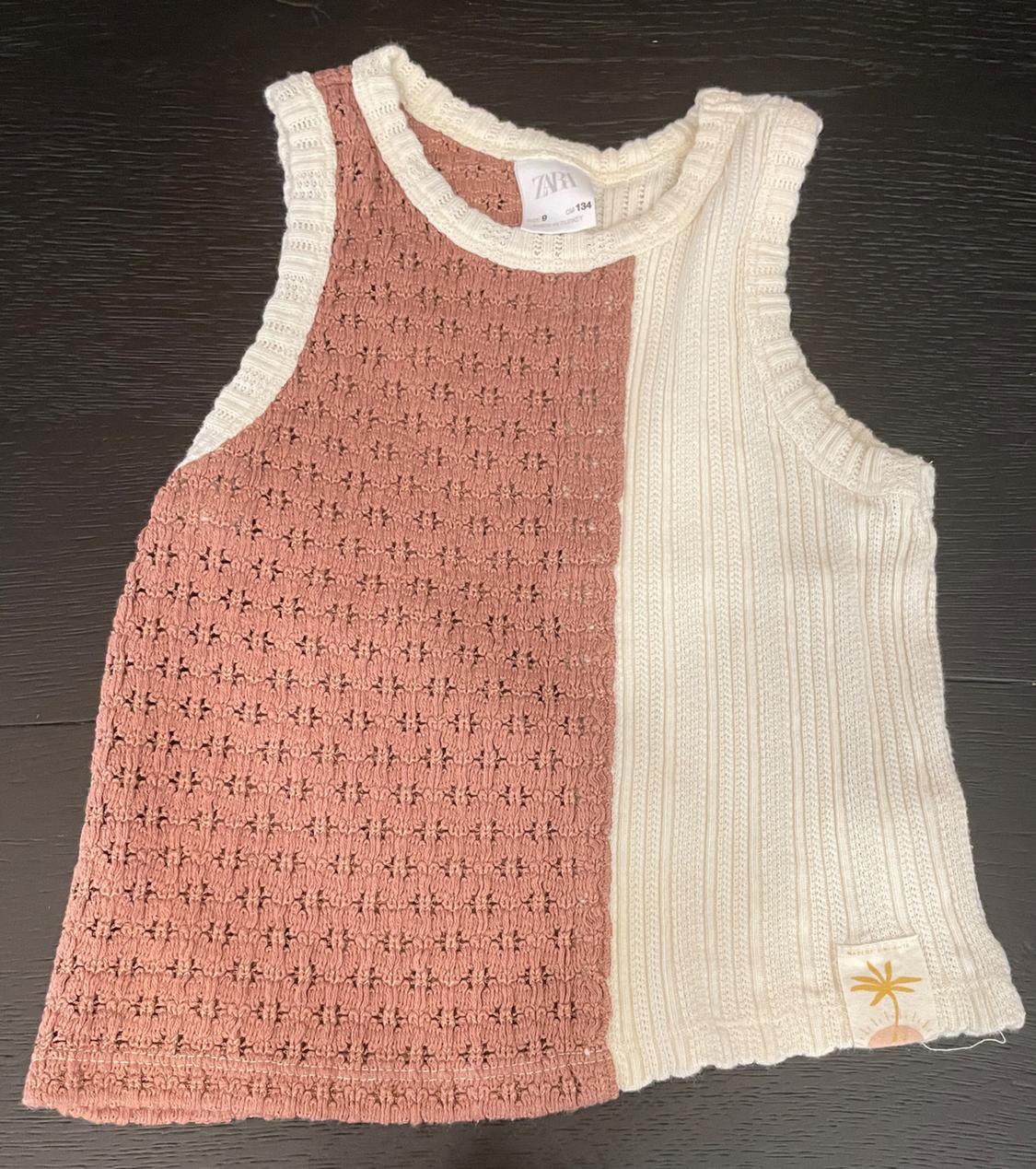 Sleeveless knit top on wood. Half pink openwork and half cream ribbed knit with a palm tree patch. Text: ZARA 9 cm 134.