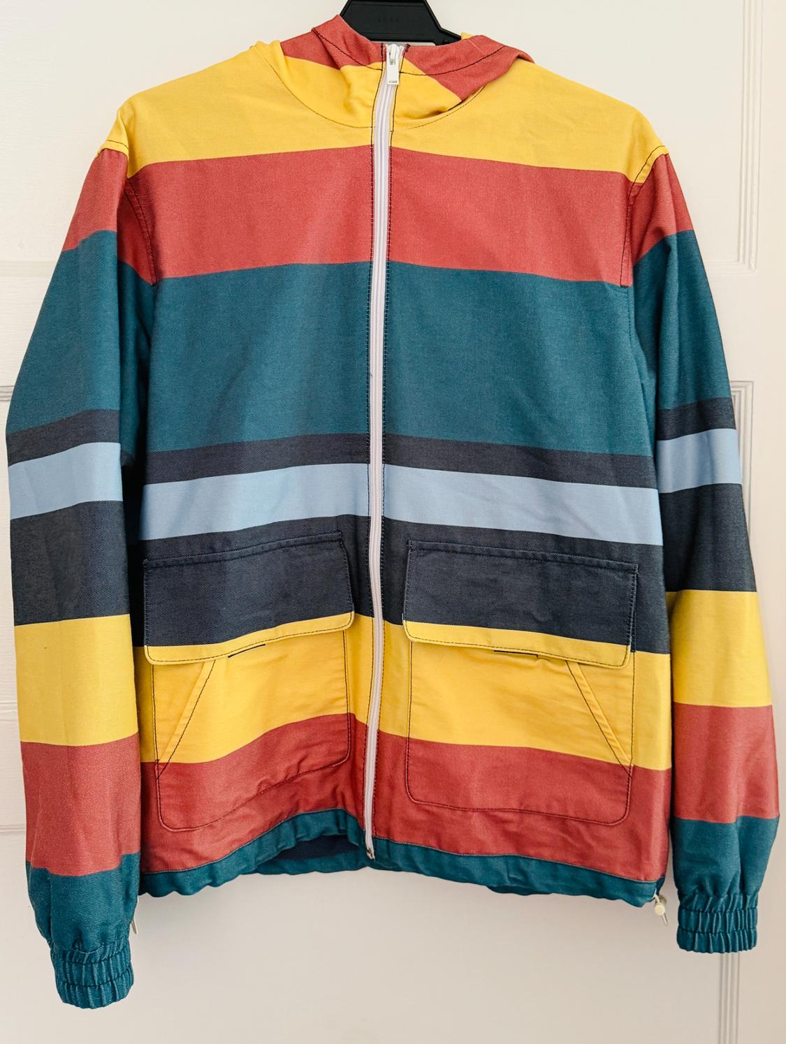 Horizontal striped hooded jacket in yellow, red, green, and blue. It has a front zipper and pockets, hanging on a white door.