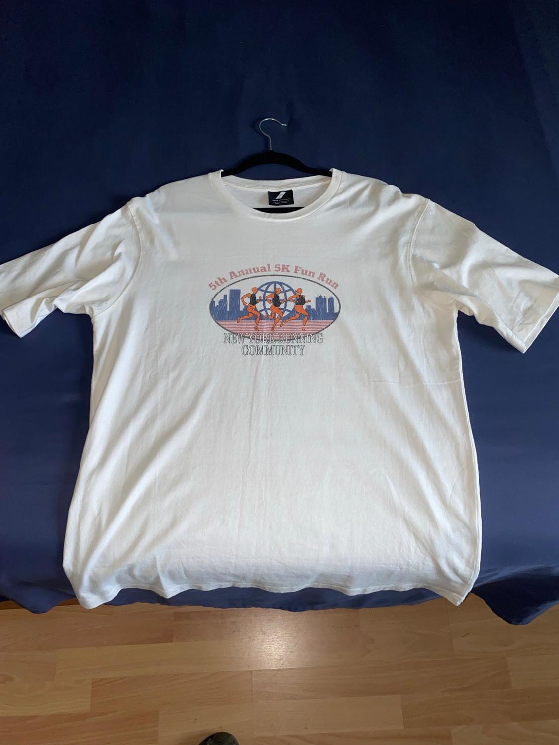 White T-shirt with the text “5th Annual 5K Fun Run NEW YORK RUNNING COMMUNITY” and a graphic of runners, on a blue surface.