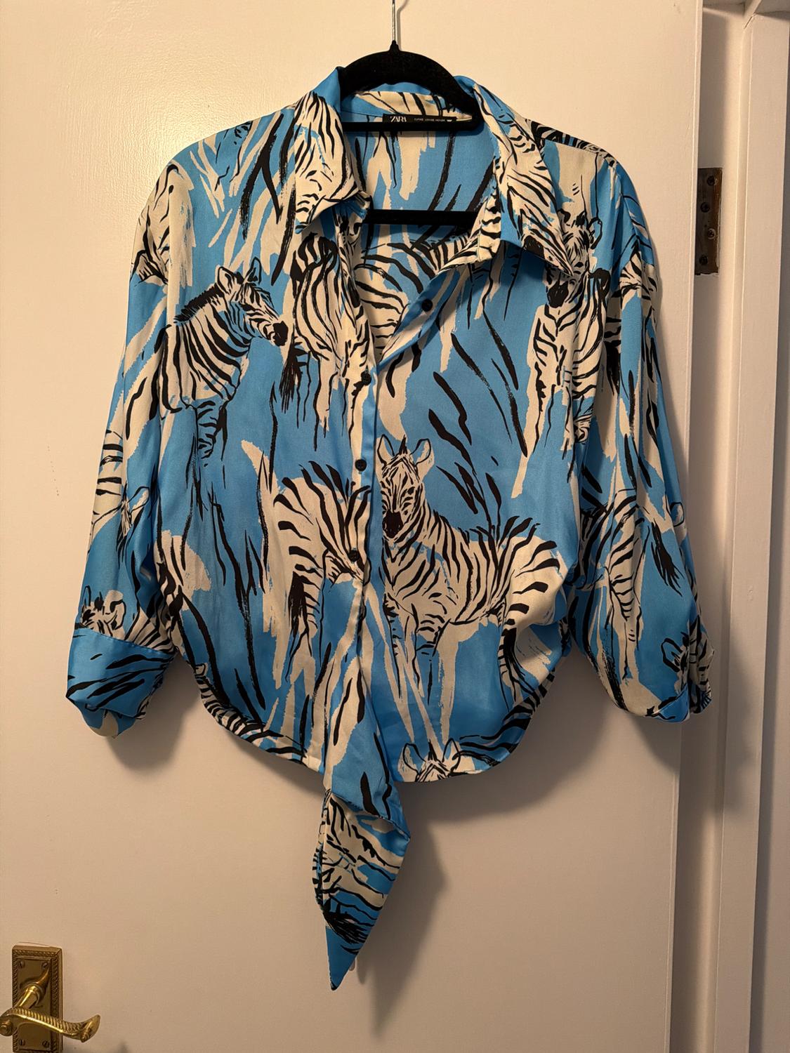 Blue shirt with a black and white zebra print, hanging on a black hanger over a white door.