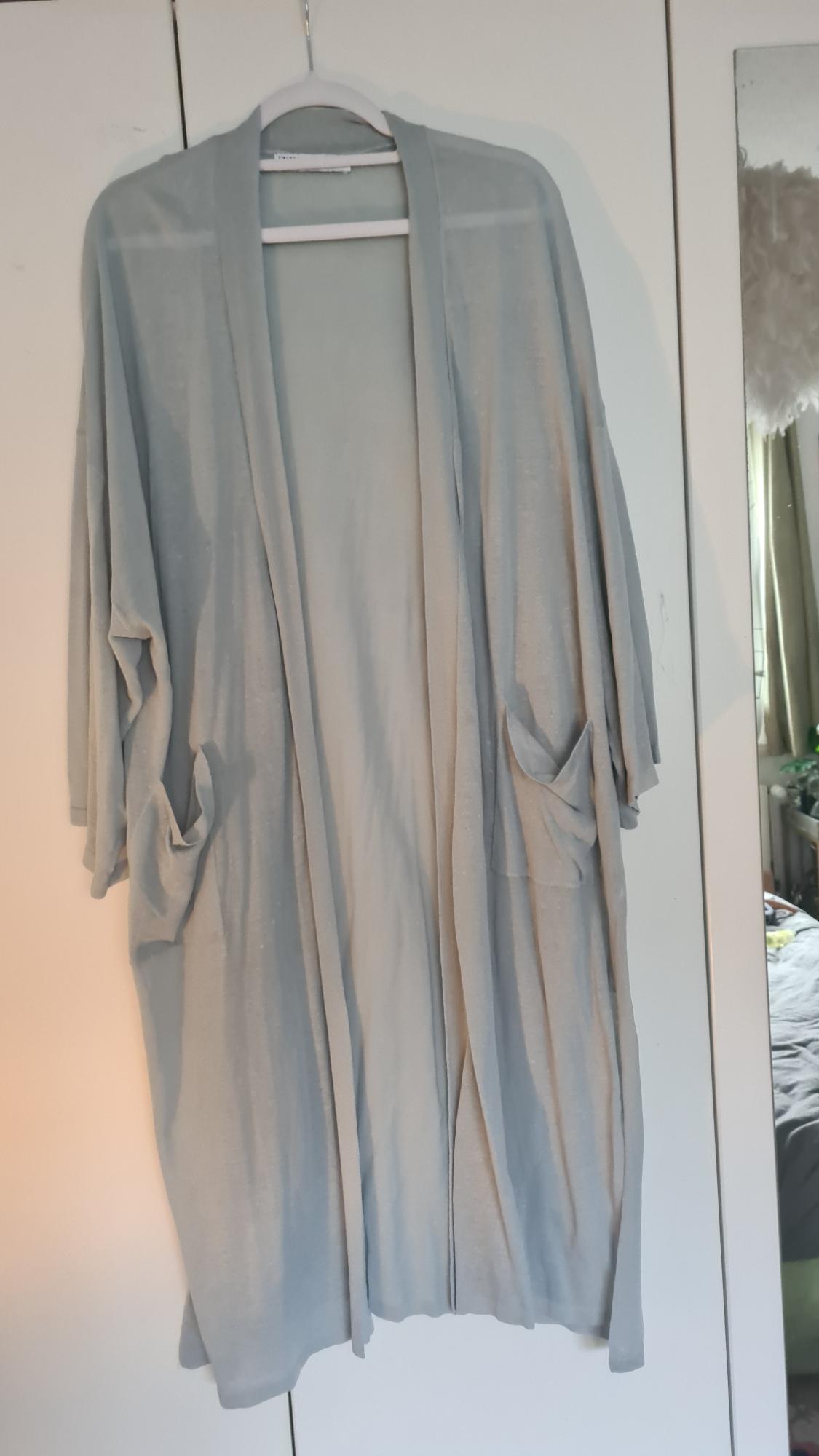 Light grey cardigan hanging on a white hanger in front of a wardrobe. Partial reflection of a room in the mirror on the right.