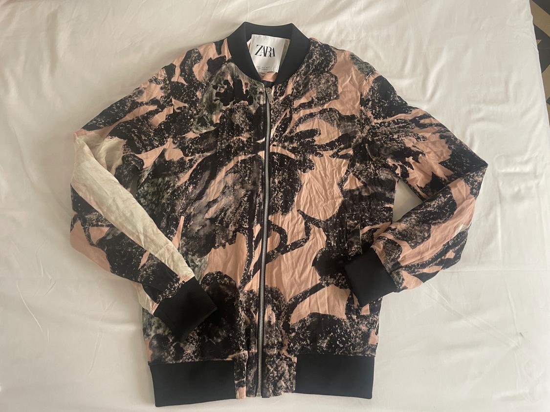 Pink and black abstract print bomber jacket with a zip, black collar and cuffs, on white fabric. Visible ZARA label.