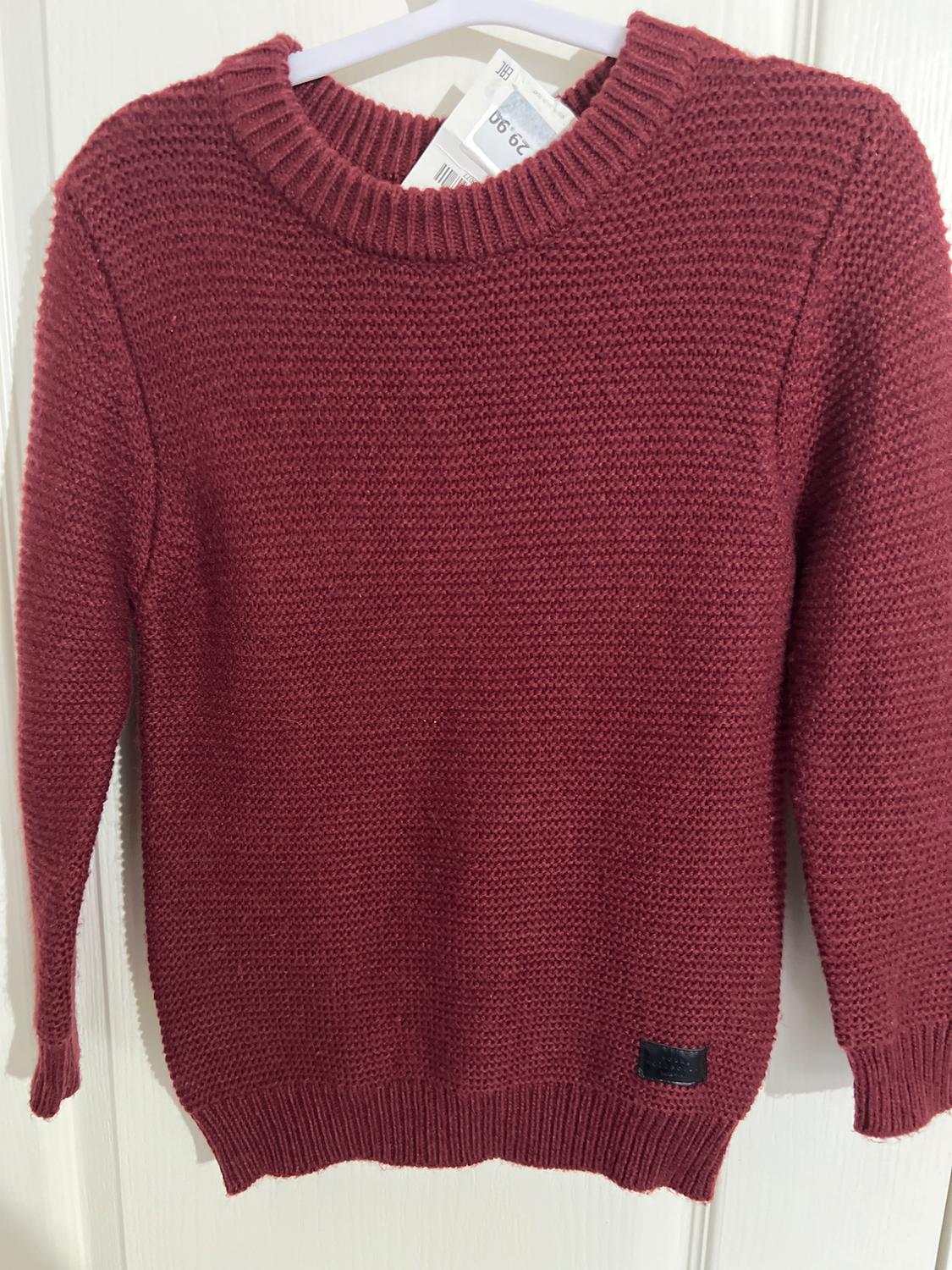 Burgundy knit sweater hanging on a white hanger. Visible tag with price of 29.99. White background.