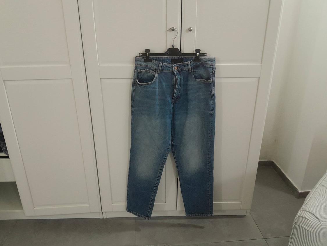 Worn blue jeans hanging on a black hanger in front of a white wardrobe in a room with grey tiled flooring.