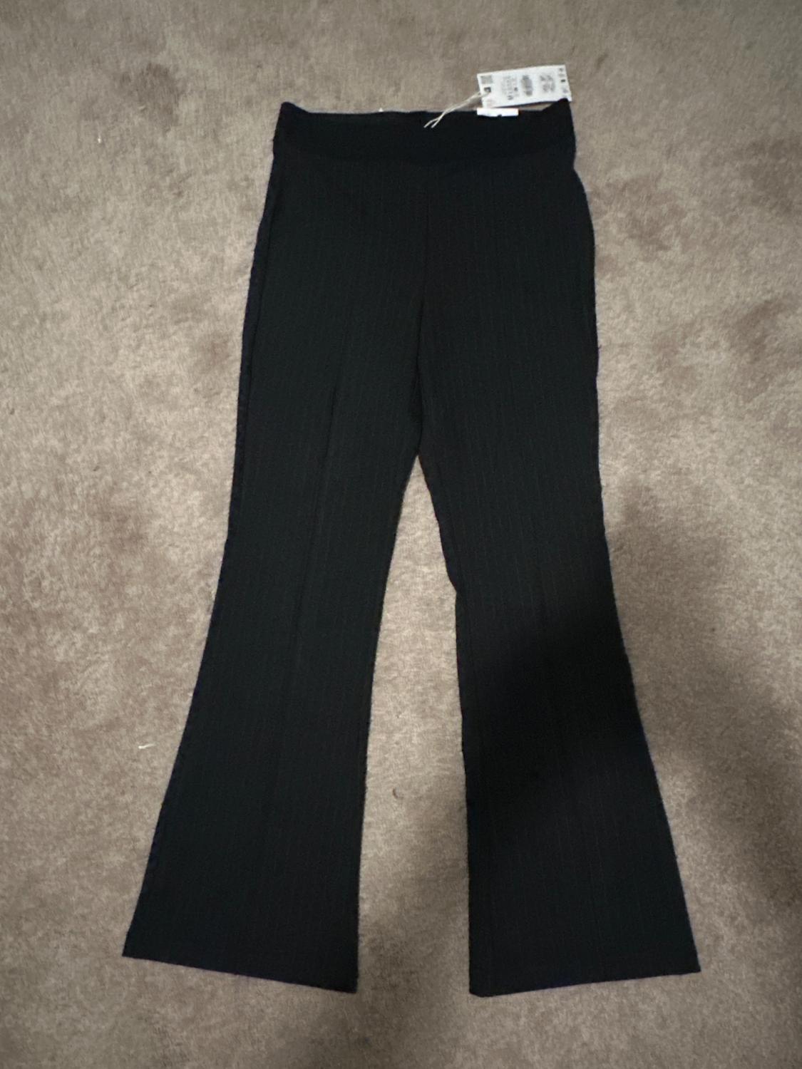 Black flared trousers on a beige carpet, with a visible label on the waistband.